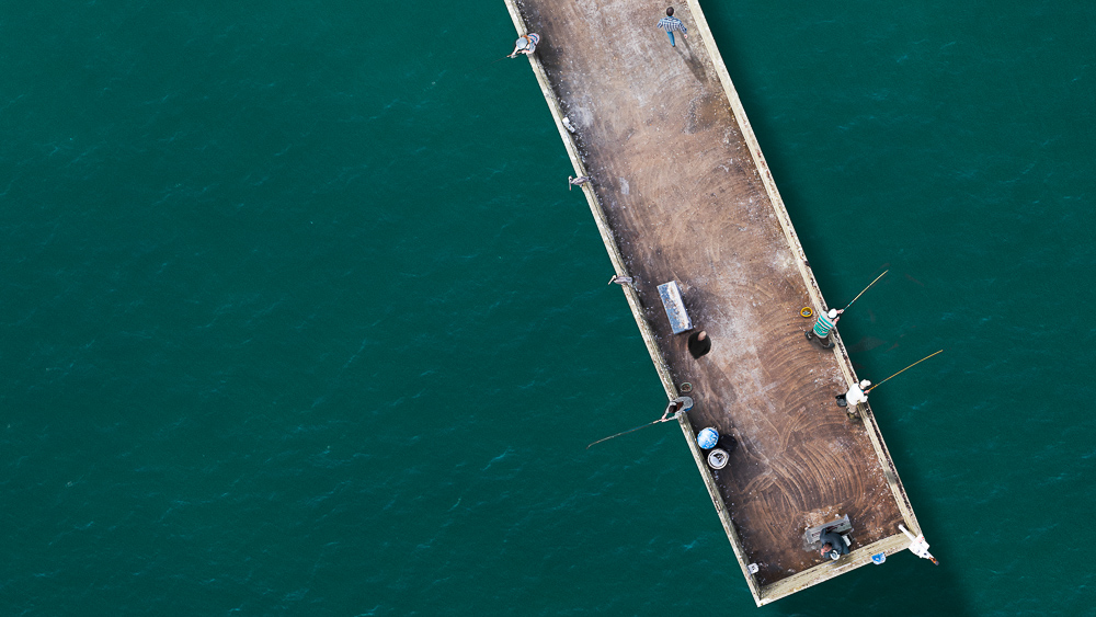 fishermen and women on ocean beach pier viewed from above