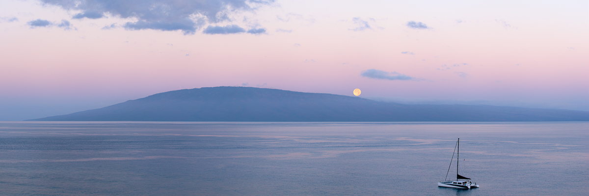full moon setting over lanai island with boat in foreground