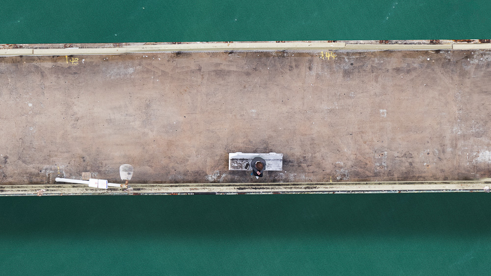 person on bench on ocean beach pier viewed from above