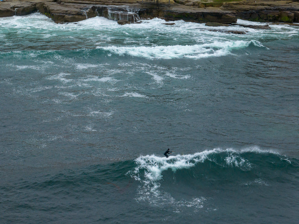 surfer on wave at windansea beach with coast in background